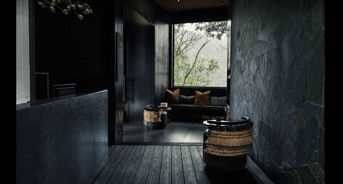 Elegant Silverback Lodge reception with natural textures and panoramic Bwindi rainforest views through a large window.