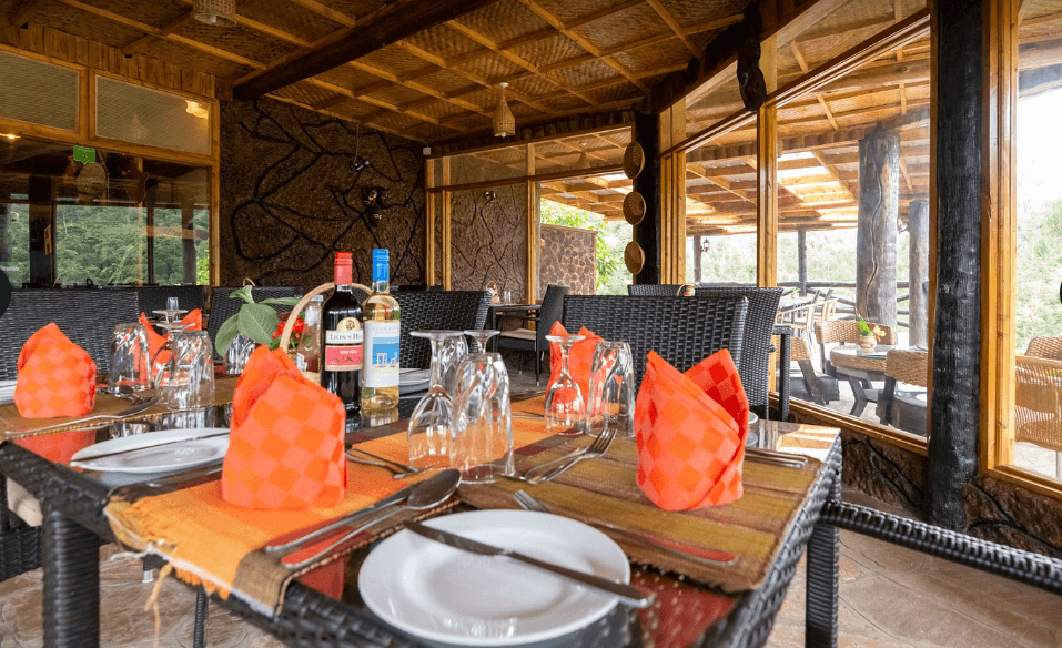 Rushaga Gorilla Camp dining area with beautifully set tables, woven interiors, large windows, and a warm forest lodge atmosphere for guests